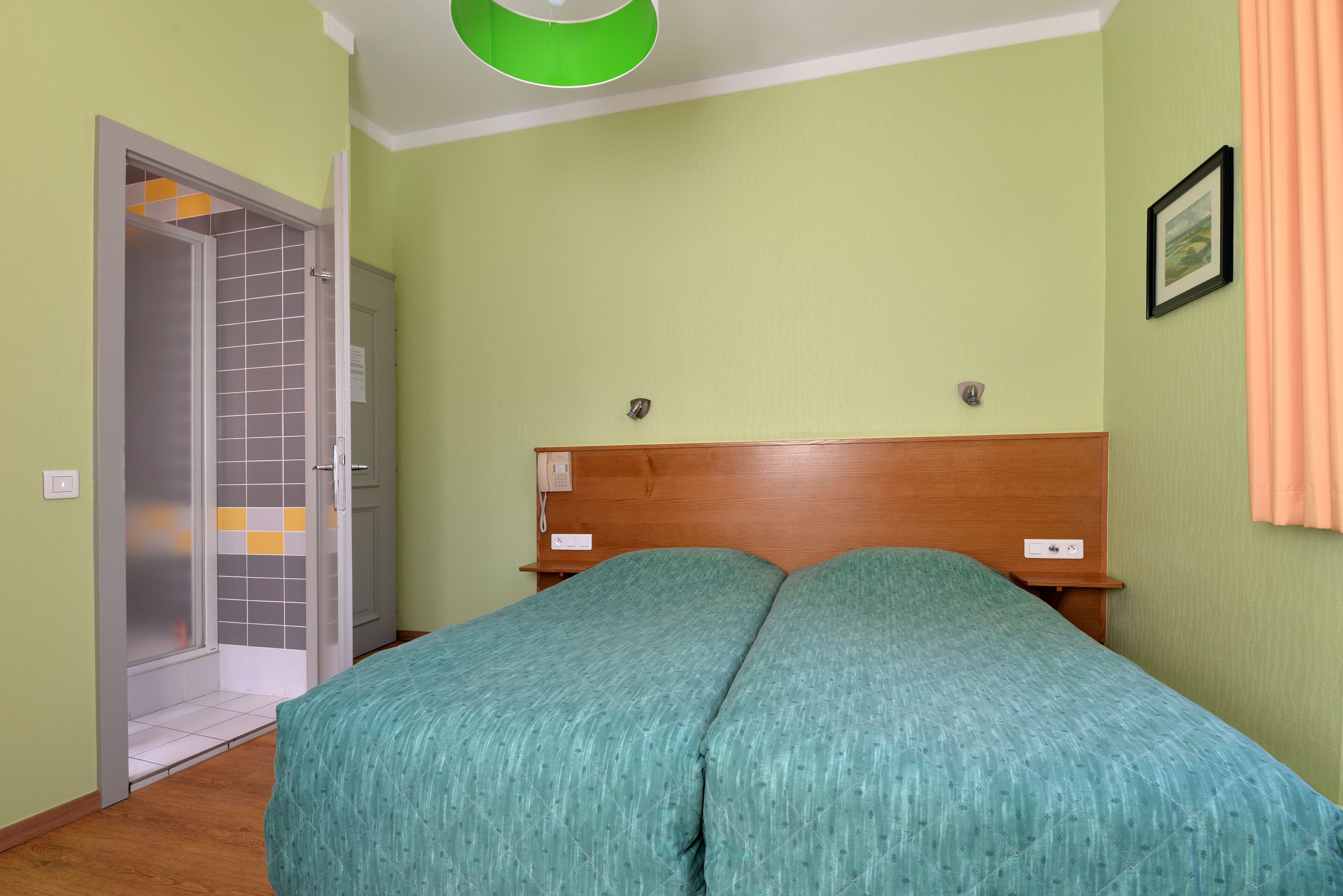 A bedroom with a wooden headboard, a green bedspread, and a door leading to a bathroom with a tiled shower area.
