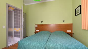 A bedroom with a wooden headboard, a green bedspread, and a door leading to a bathroom with a tiled shower area.