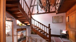 Una escalera de madera con barandilla de hierro forjado, un candelabro y vistas de un castillo a través de una ventana.