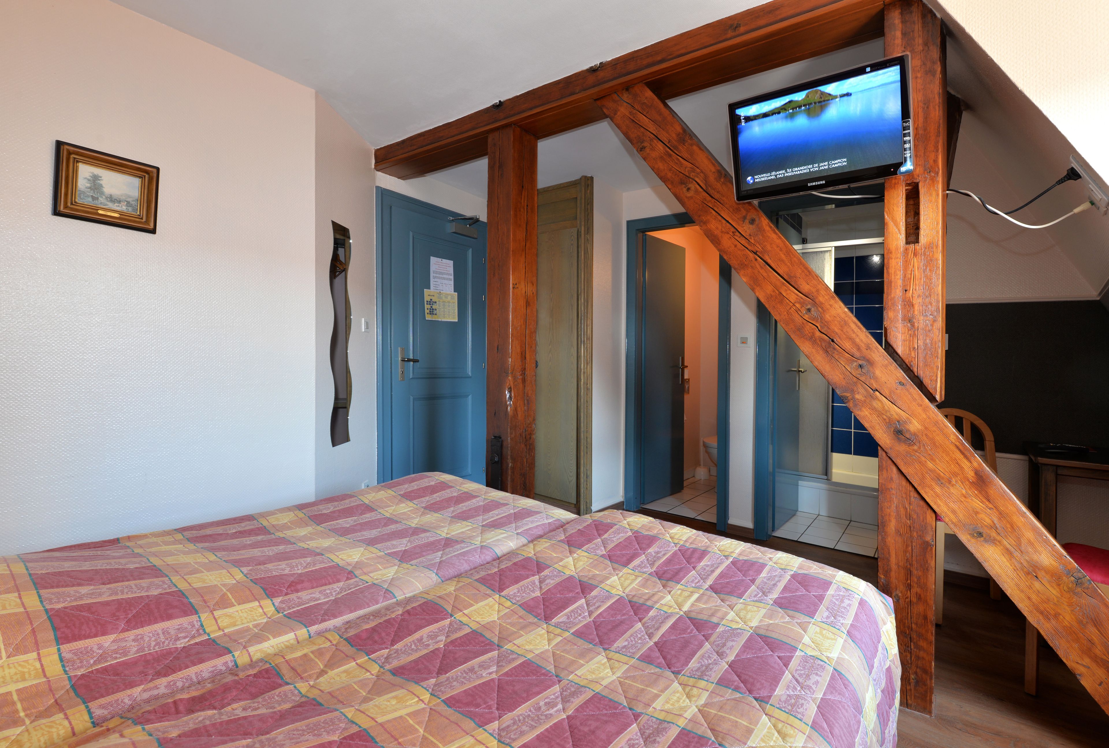 Une chambre à coucher avec un lit, un téléviseur fixé sur une poutre en bois et une porte donnant sur une autre pièce.