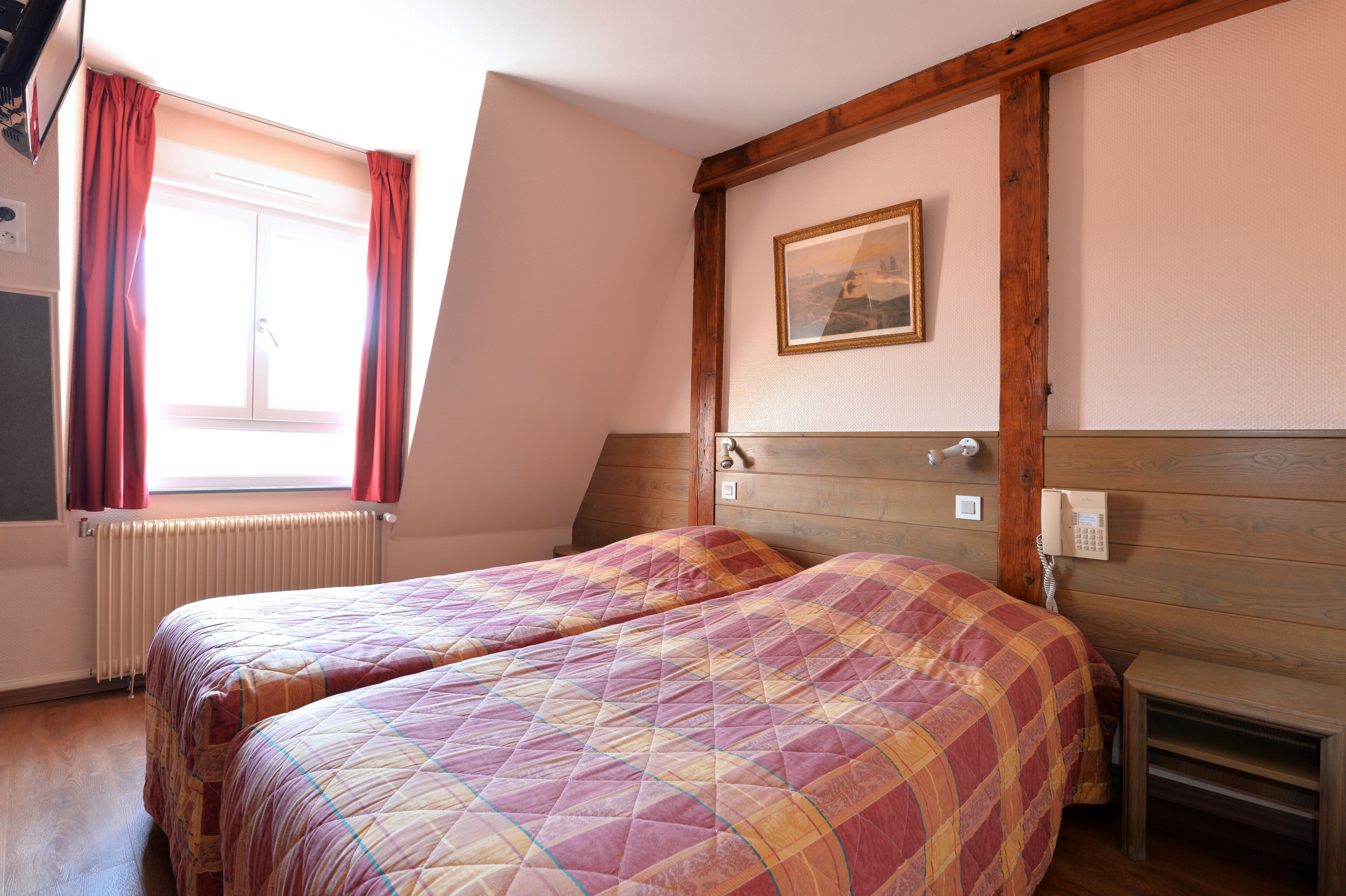 Un dormitorio con dos camas, cabeceros de madera, un cuadro en la pared y una ventana con cortinas.