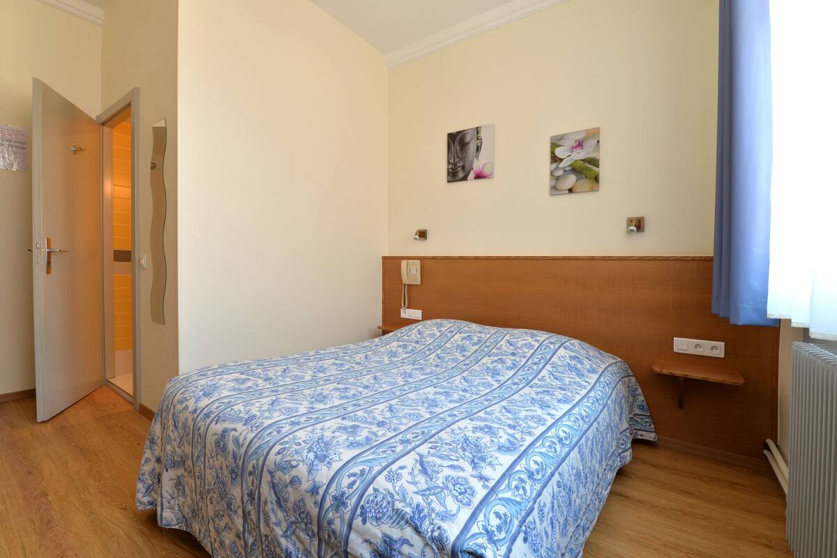 Un dormitorio con cama, piso de madera, una puerta y una pared con dos cuadros.