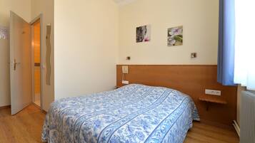 A bedroom with a bed, wooden floor, a door, and a wall with two pictures.