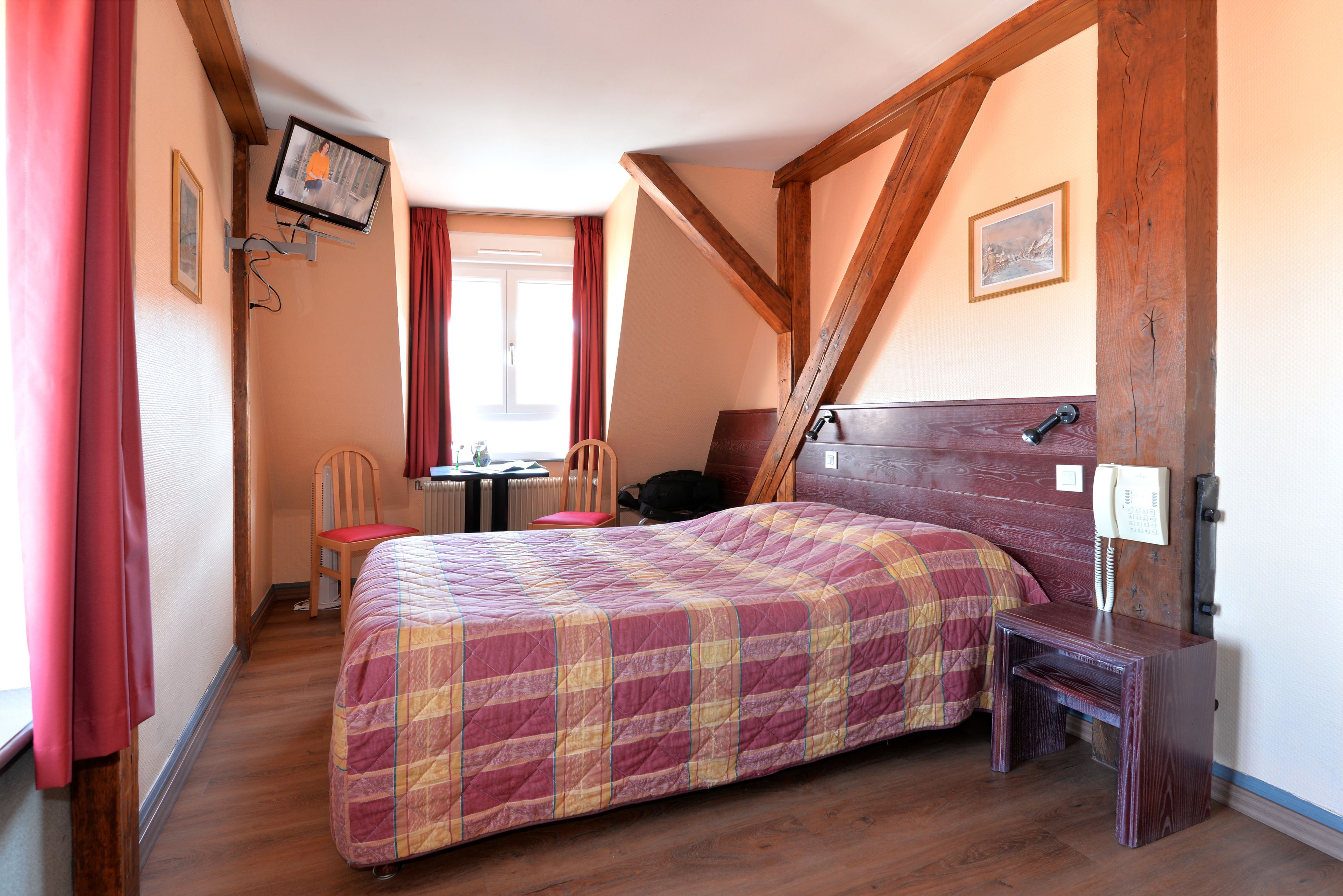 Een slaapkamer met een groot bed, een houten hoofdbord, een aan de muur bevestigde televisie en een tafeltje met een telefoon.