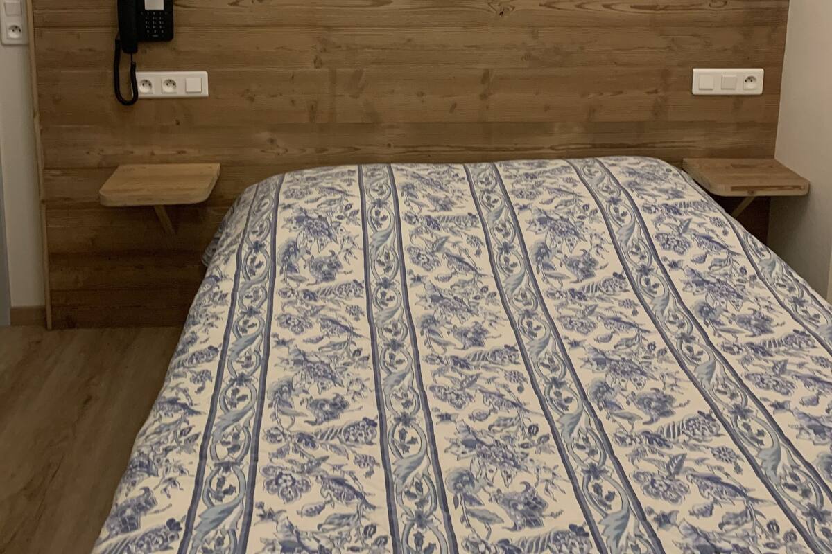 Un dormitorio con cabecera de madera, edredón estampado, dos mesitas de noche, un teléfono y dos cuadros en la pared.