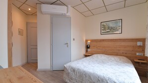 Un dormitorio con cabecera de madera, una cama con colcha blanca, una mesita de noche y un teléfono en la pared, además de un cuadro.