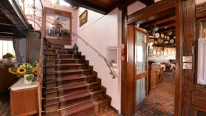 Una escalera de madera con alfombra estampada que conduce a una habitación con suelo de baldosas y vistas a un comedor.