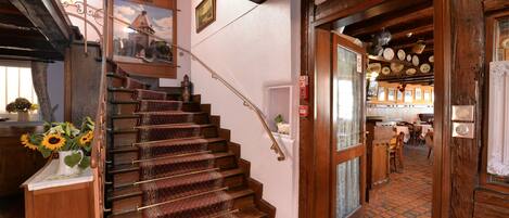 A wooden staircase with patterned carpet leading to a room with a tiled floor and a view of a dining area.