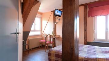 Un dormitorio con cama, escritorio con silla, televisor montado en la pared y ventana con cortina roja.