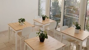 Una habitación luminosa con techo de cristal, paredes blancas y varias mesas con sillas y plantas en macetas.