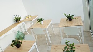 Una habitación moderna y limpia, con paredes blancas y mesas de madera. Hay plantas en macetas sobre las mesas y un jarrón verde en el suelo.
