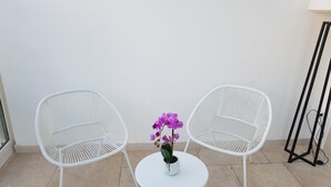 Dos sillas de mimbre blancas con una mesita pequeña y una orquídea en maceta en el centro.