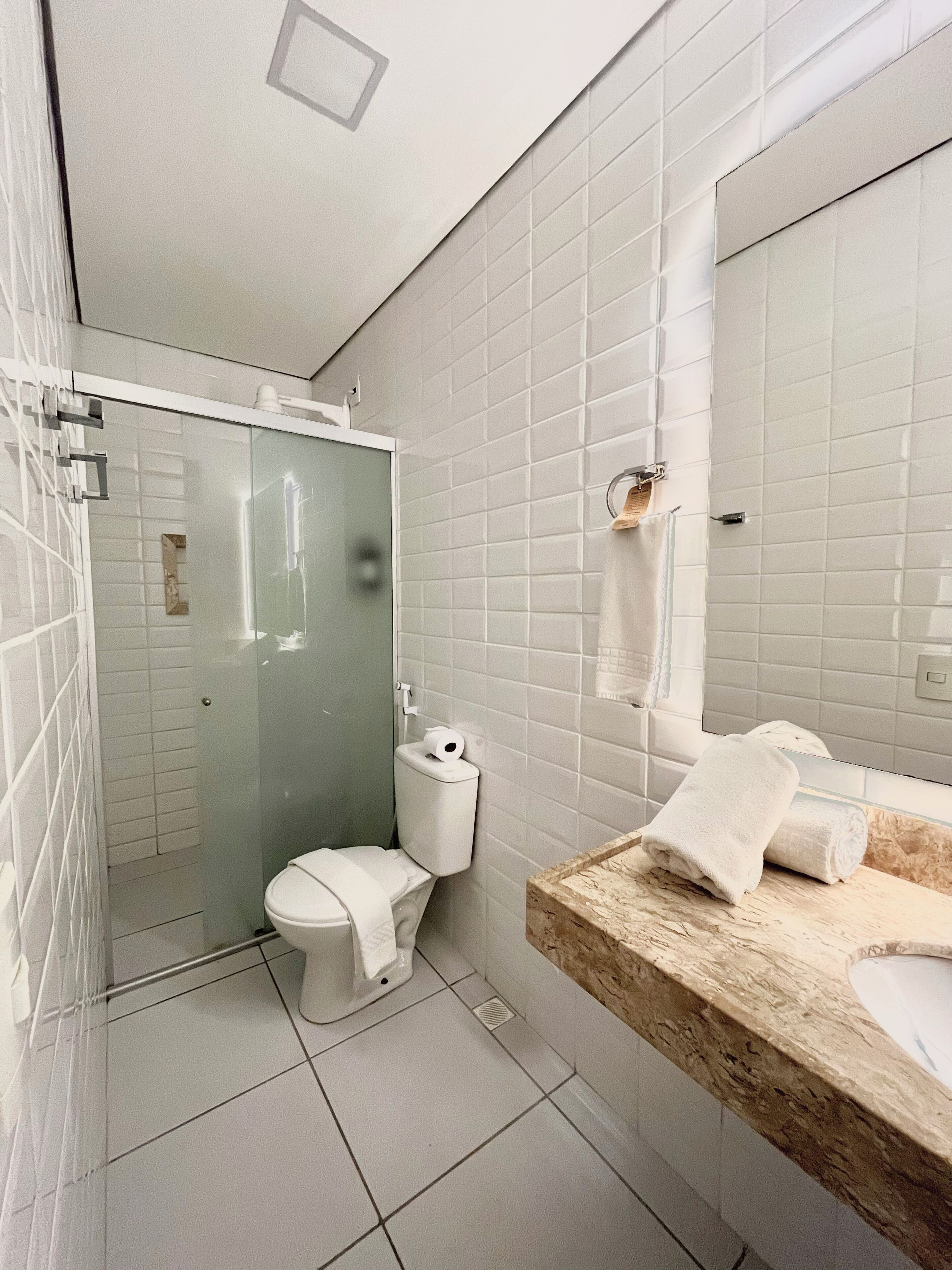 Une salle de bain moderne avec des carreaux blancs, une douche en verre, des toilettes et un lavabo doté d’un plan de travail en marbre.