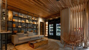A modern living room with a sofa, coffee table, and wicker chair. There are shelves with decorative items and a door leading to another room. - Pauli Boutique Hotel  (Fortaleza)