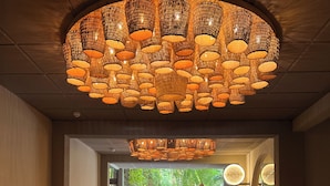A stone-tiled hallway with a large woven ceiling light fixture and a view of lush greenery outside. - Pauli Boutique Hotel  (Fortaleza)