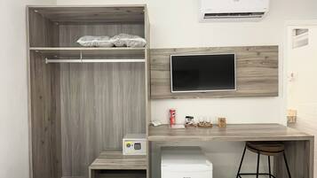 Una habitación de hotel moderna con un armario de madera, una pequeña cocina americana, un televisor montado en la pared y un refrigerador compacto.