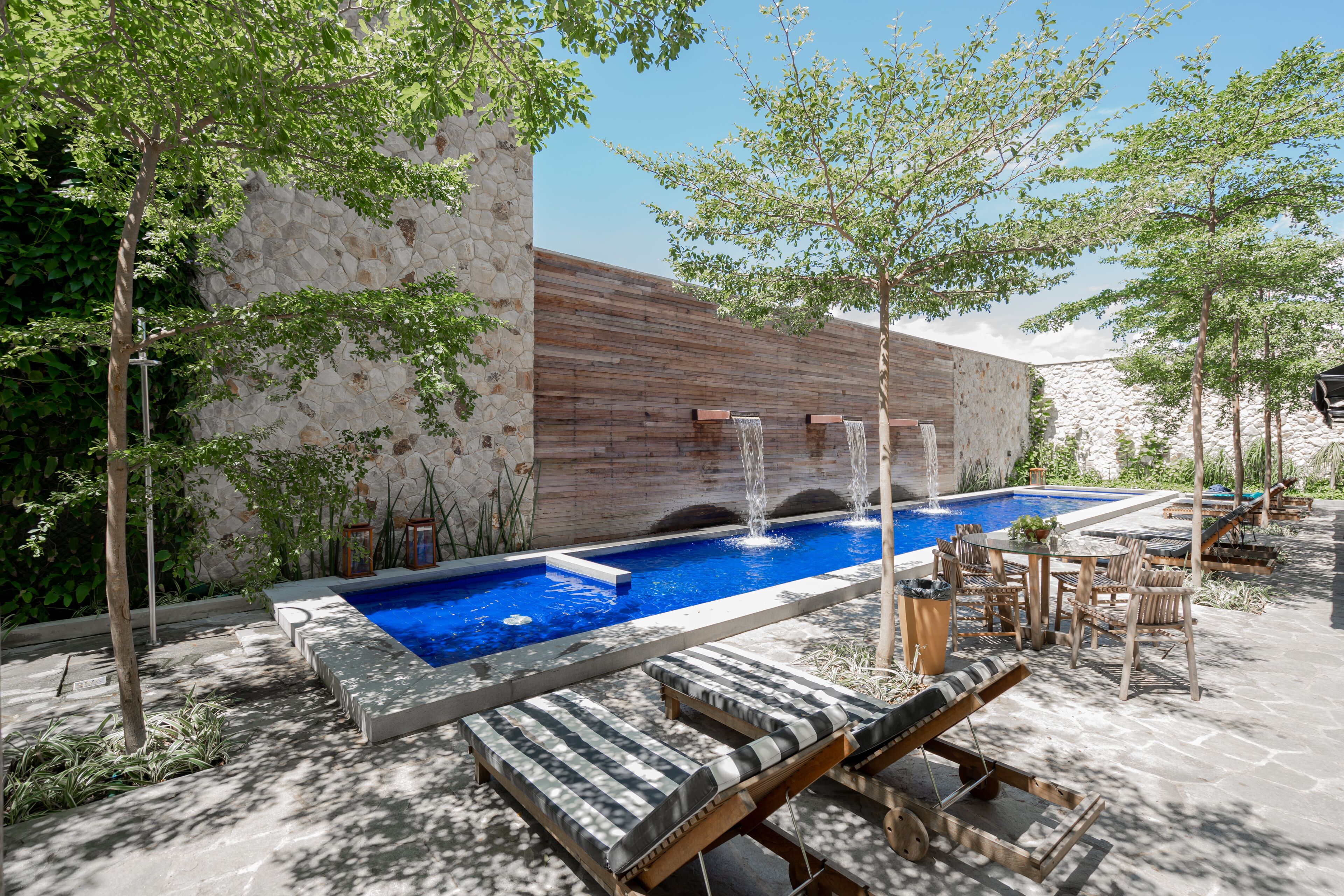 Un espace piscine agrémenté d’un mur en pierre, de chaises longues et d’une terrasse en bois.