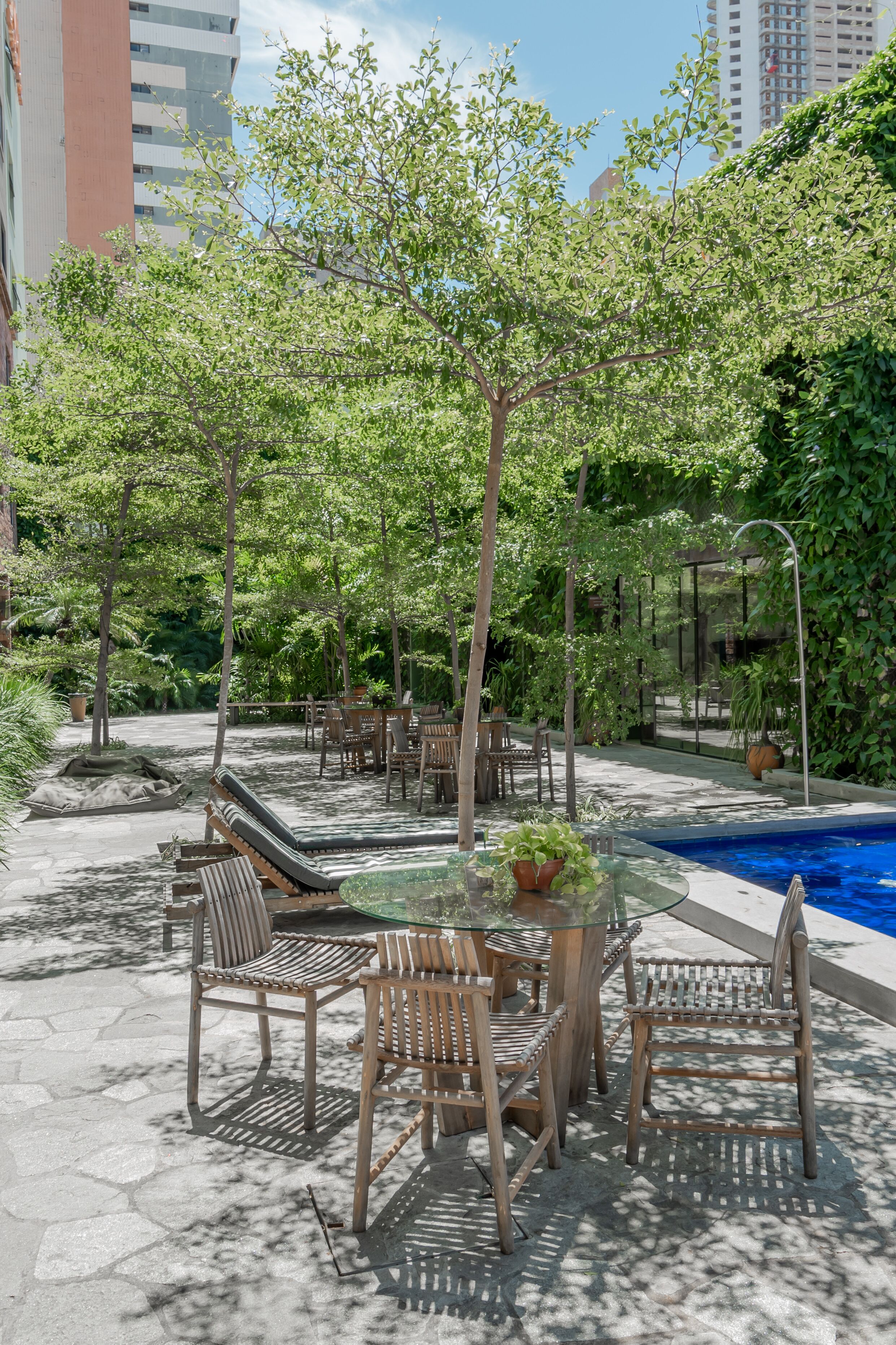 Zona de piscina exterior con sillones de descanso y una mesa de vidrio rodeada de vegetación.