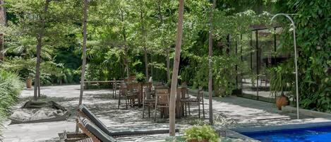 Zona de piscina exterior con sillones de descanso y una mesa de vidrio rodeada de vegetación.
