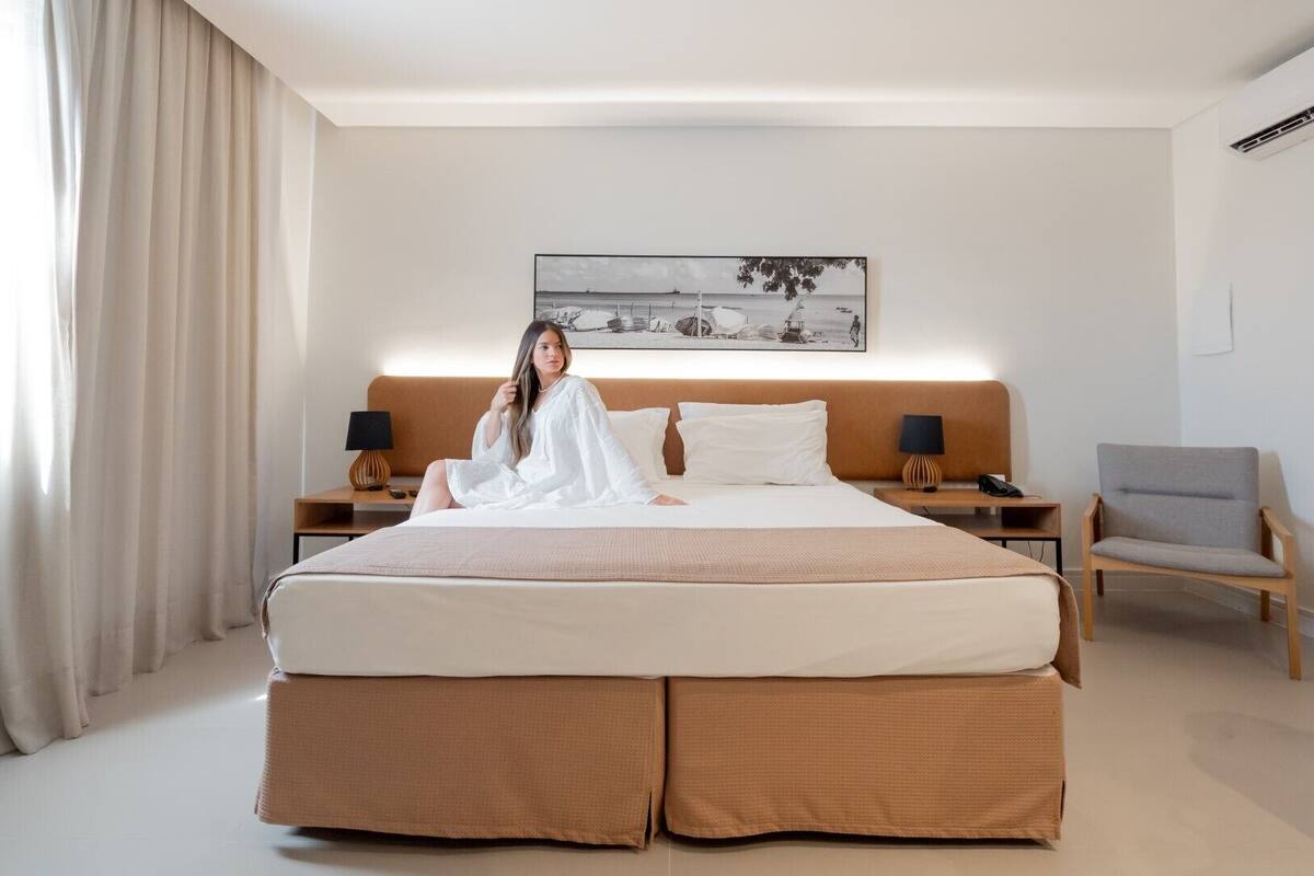 A modern hotel room with a large bed, two bedside tables, a chair, and a painting on the wall.