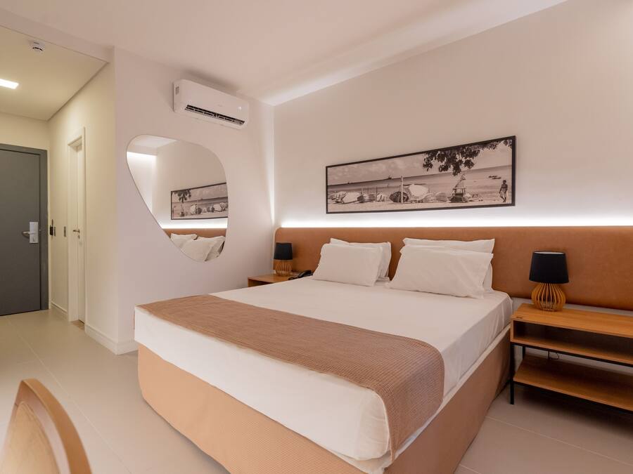 Habitación de hotel moderna con una cama grande, una mesita de noche con lámpara, aire acondicionado montado en la pared y un cuadro enmarcado sobre la cama.
