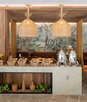Montaje de buffet con cestas de mimbre, una estación de café y un área de estar con un mural de plantas tropicales.