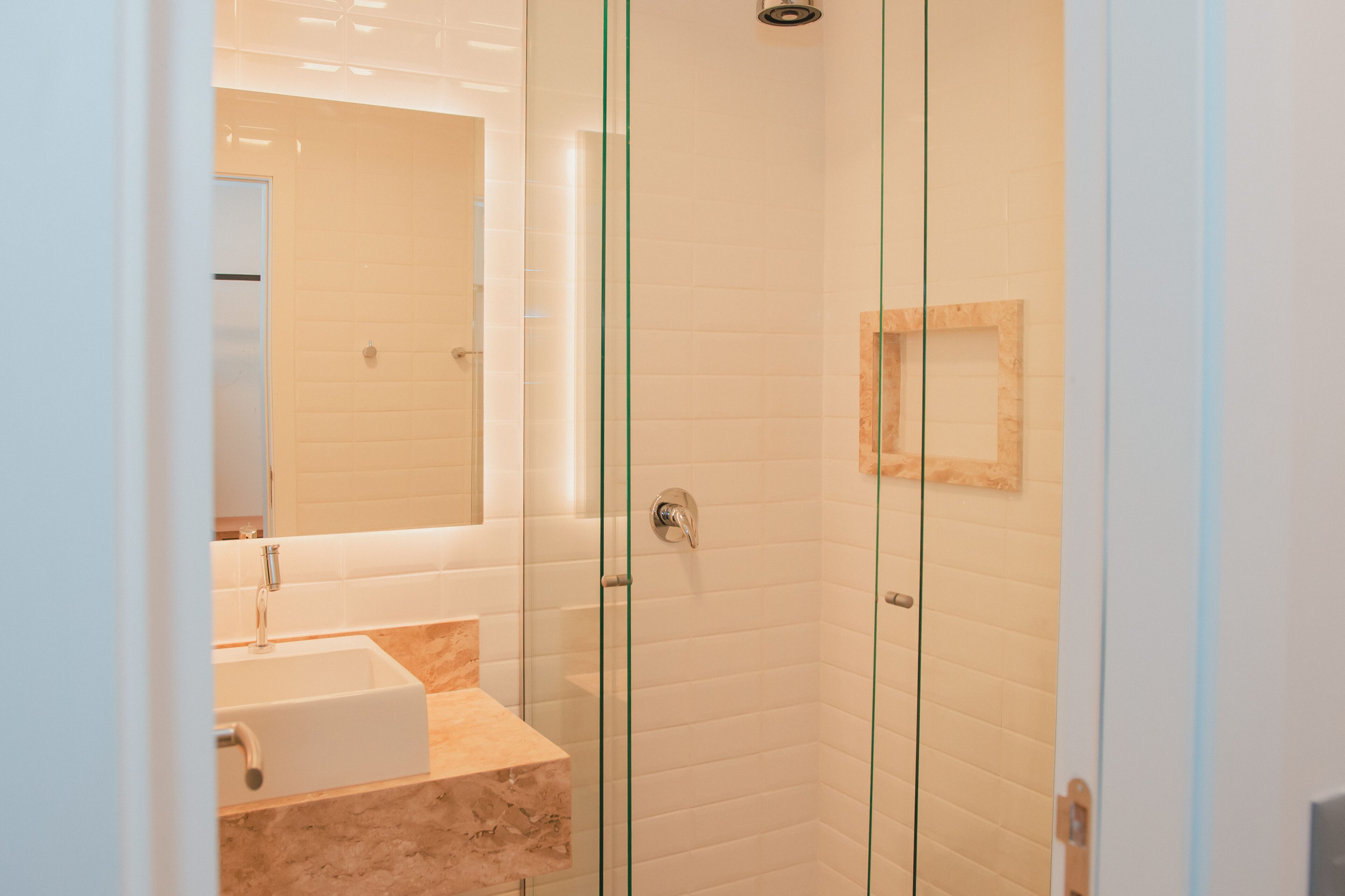 A modern bathroom with a glass shower enclosure, a sink with a marble countertop, and a mirror.