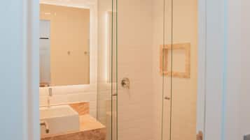Un baño moderno con cabina de ducha de vidrio, un lavabo con encimera de mármol y un espejo.