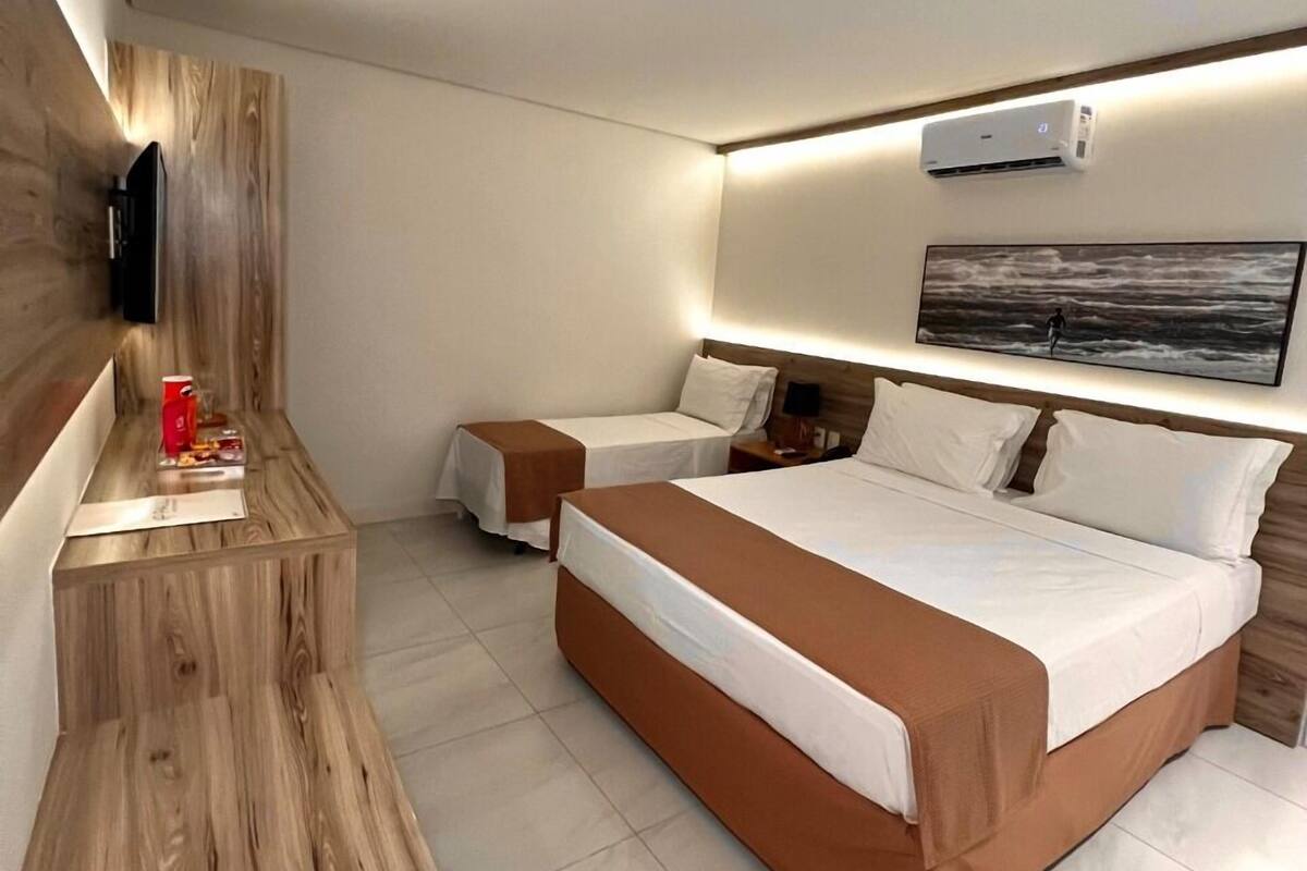 A modern hotel room with a large bed, a bedside table, a TV, and a painting on the wall.