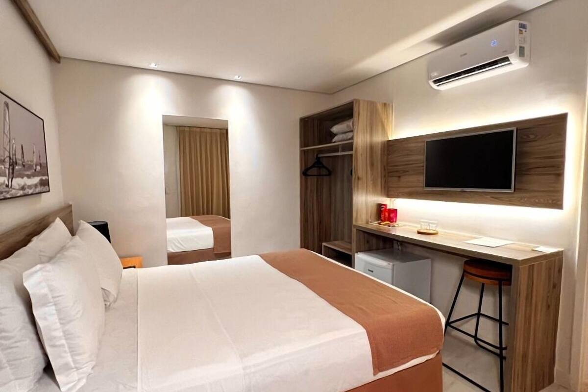 A modern hotel room with a large bed, a desk with a chair, a TV, and a wardrobe.