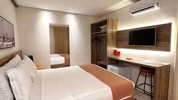 Una habitación de hotel moderna con una cama grande, un escritorio con silla, un televisor y un armario.