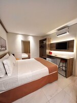 Una habitación de hotel moderna con una cama grande, un escritorio con silla, un televisor y un armario.