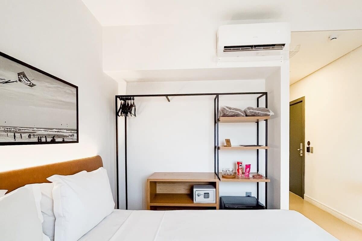 A hotel room with a bed, a wardrobe, a shelf with toiletries, and a framed picture on the wall.