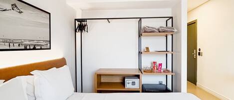 A hotel room with a bed, a wardrobe, a shelf with toiletries, and a framed picture on the wall.