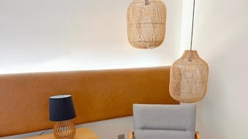 A modern room with a wooden bench, a grey chair, and two woven pendant lights.