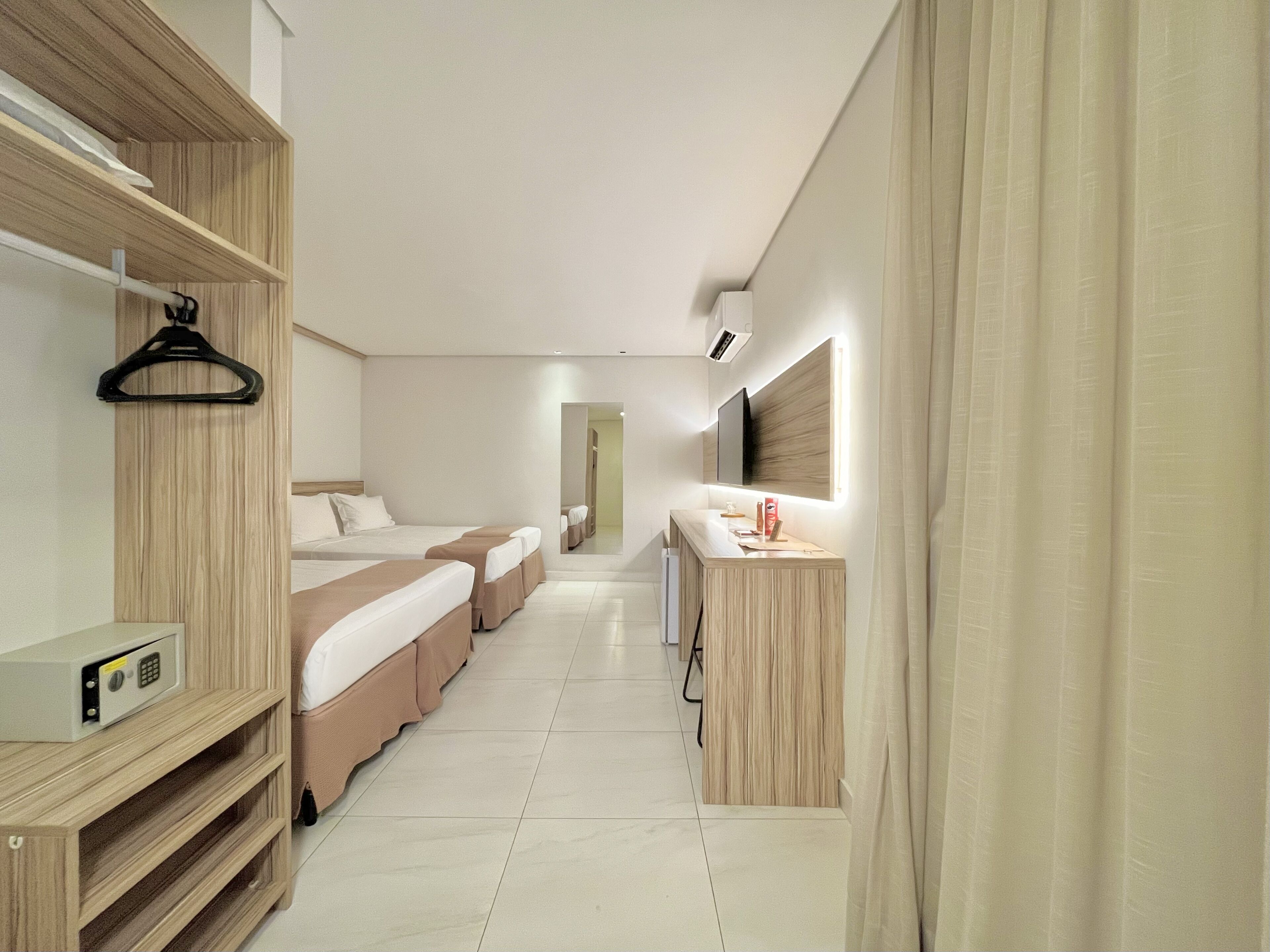 A hotel room with a long corridor, wooden furniture, a desk with a mirror, and a bed with a headboard.