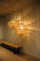 Una habitación con un banco de madera y dos lámparas tejidas frente a una pared con textura.