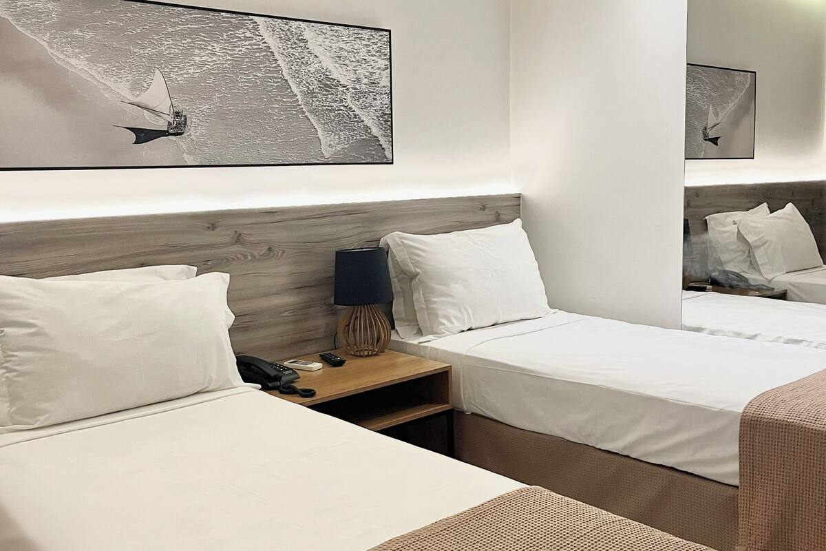 A modern hotel room with two beds, a nightstand with a lamp, and a large abstract painting on the wall.