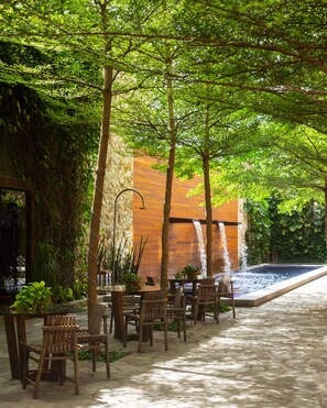 An outdoor seating area with tables and chairs, a stone wall, and a small water feature. - Pauli Boutique Hotel  (Fortaleza)