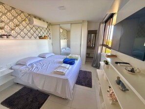 Een moderne slaapkamer met een bed, nachtkastjes, een televisie en een zichtbare badkamer door een open deur.