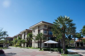 Een meerhoog hotel met een centrale binnenplaats, palmbomen en een overdekt zitgedeelte.