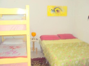 Una cama litera con ropa de cama rosa, una mesita con una lámpara y una colcha estampada con motivos florales.