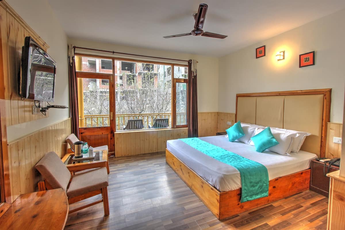 A bedroom with a large bed, wooden headboard, a ceiling fan, a TV mounted on the wall, and a window with a view of buildings.