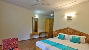 Habitación de hotel con cama de madera, escritorio, silla, armario y ventilador de techo.