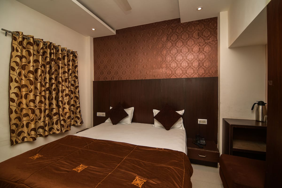 A hotel room with a large bed, a wooden headboard, a nightstand, a coffee maker, and a curtain with a leaf pattern.