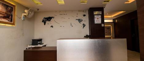 Un área de recepción con un mostrador de madera, un mapa mundial en la pared y un cartel que indica la hora de salida.