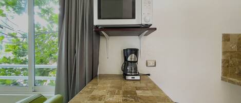 Una pequeña cocina americana equipada con microondas, cafetera y una ventana con cortinas.
