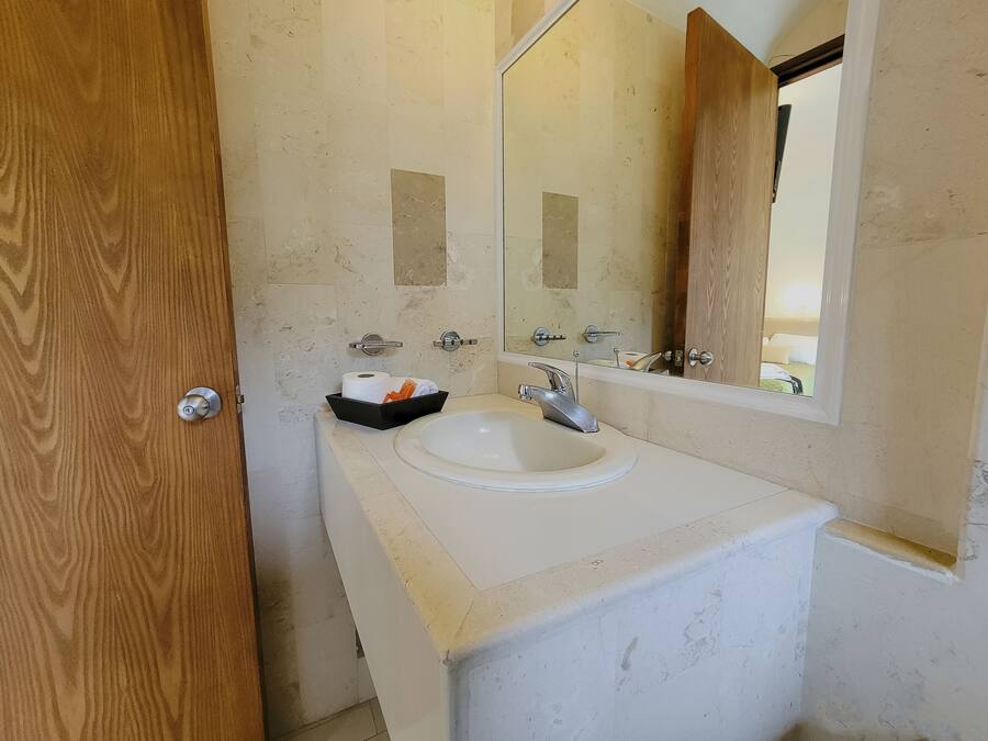 Un baño con un lavamanos blanco, un espejo y una puerta de madera.