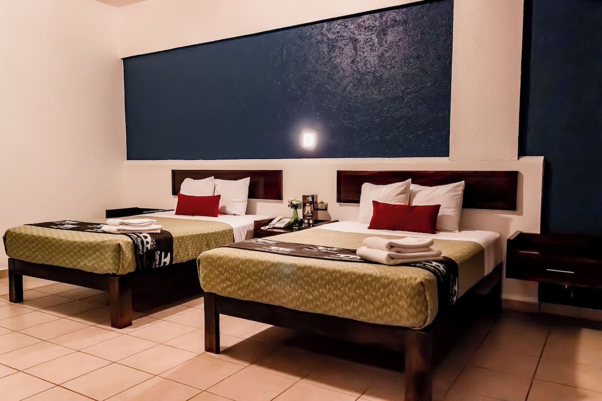A hotel room with two beds, a large dark wall, and a television.