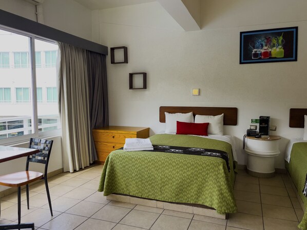 Quarto de hotel com cama, mesa de cabeceira, cadeira e vista para o exterior.